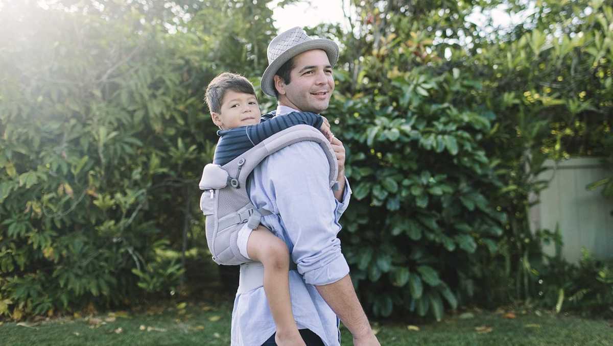 um papai carregando seu filho no canguru na costa